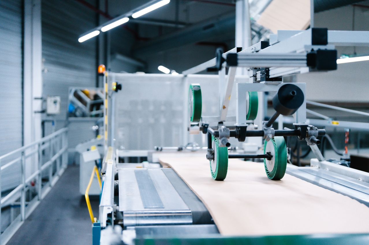 A factory conveyor belt with a machine on it, transporting a sheet of paper. The machine has green wheels and metal parts.