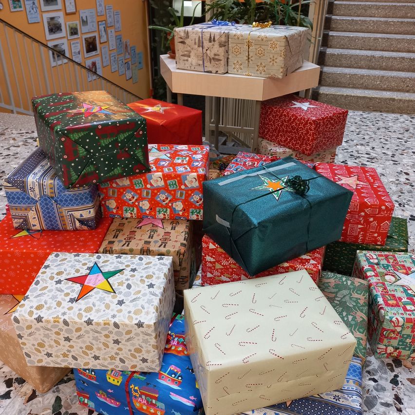 Ein Raum mit mehreren Geschenkboxen, einige mit Sternen, Süßigkeiten und anderen Designs, gestapelt auf einem gefliesten Boden in der Nähe einer Treppe und eines Schreibtisches mit Pflanzen.