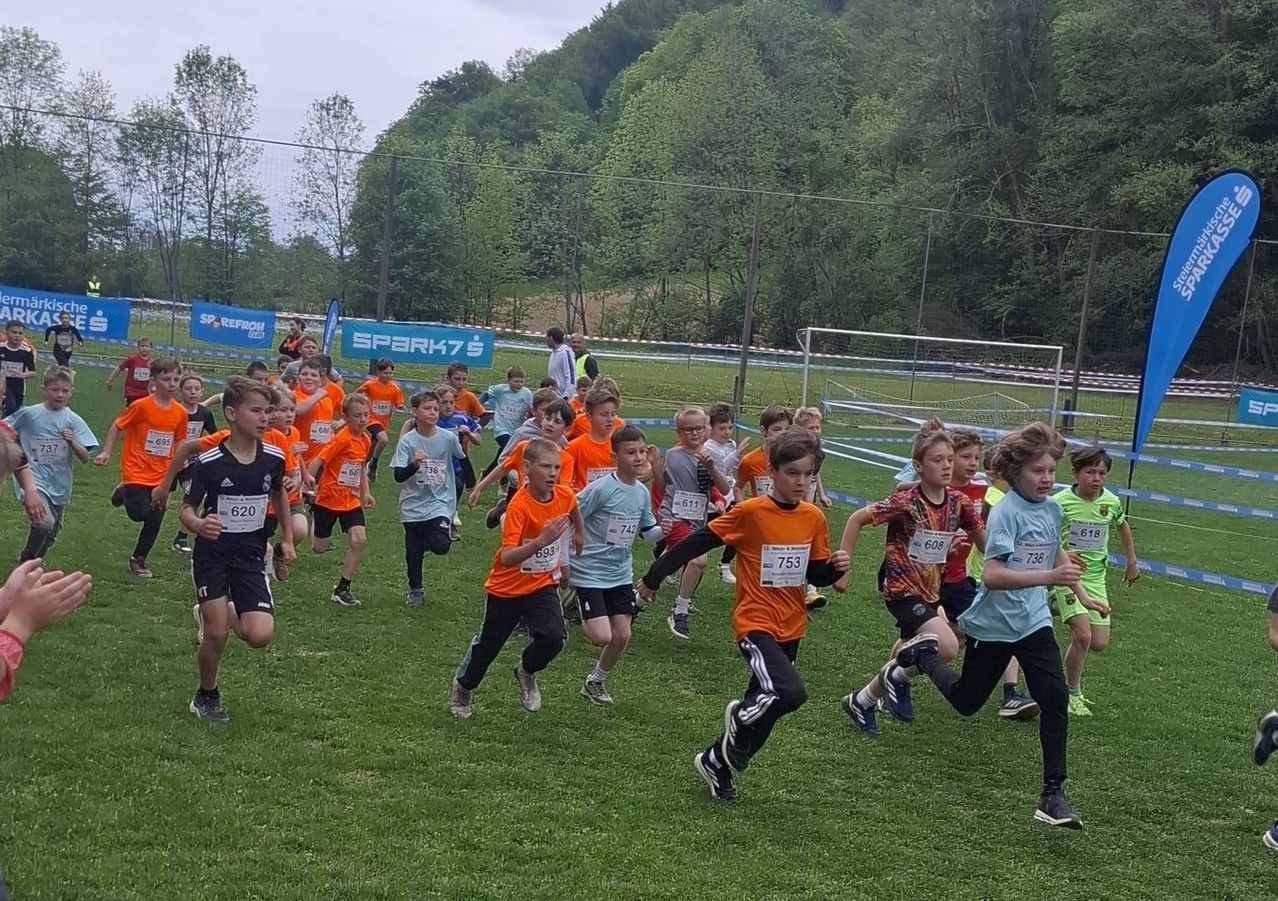 Mehrere junge Jungen nehmen an einem Laufwettbewerb auf einem Rasenfeld teil. Sie sind auf ihren Trikots nummeriert.