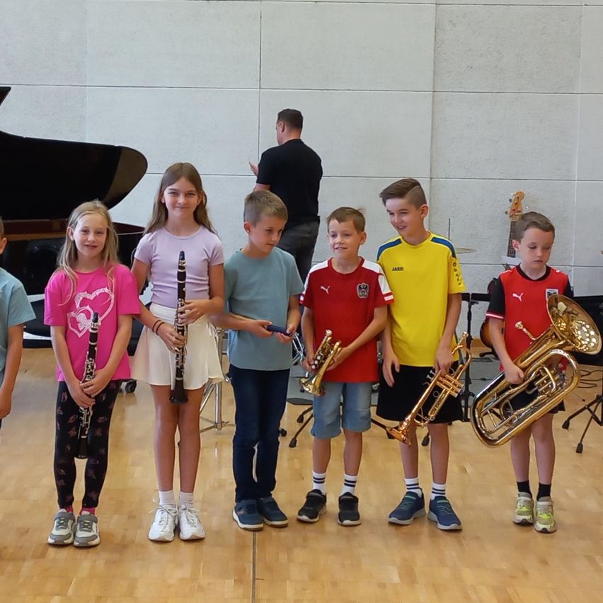 Mehrere Kinder stehen in einem Musikraum, jedes hält ein anderes Musikinstrument. Sie lächeln für ein Foto.