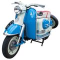 Ein altmodischer Roller mit blauer und weißer Lackierung, Scheinwerfer und einem Nummernschild, das 'DUCH SR 1190' liest. Er hat einen kleinen Reservereifen und einen Metallständer.