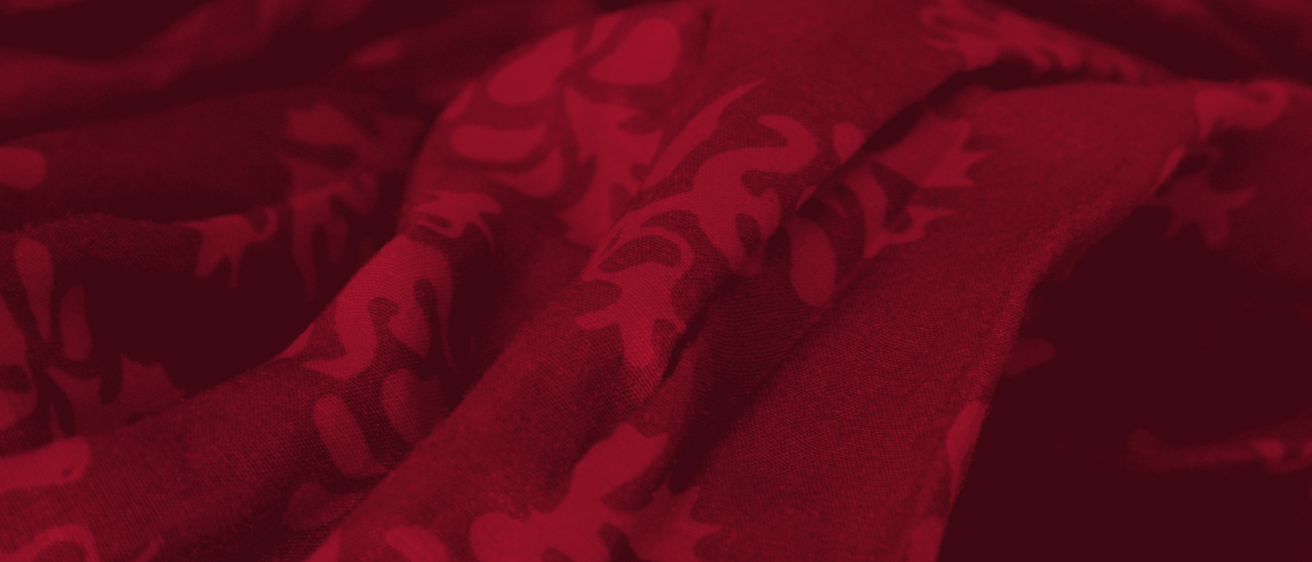 Eine Nahaufnahme eines purpurroten Stoffes mit komplizierten, abstrakten Blumenmustern. Die Textur ist weich und der Stoff erscheint leicht zerknittert.
