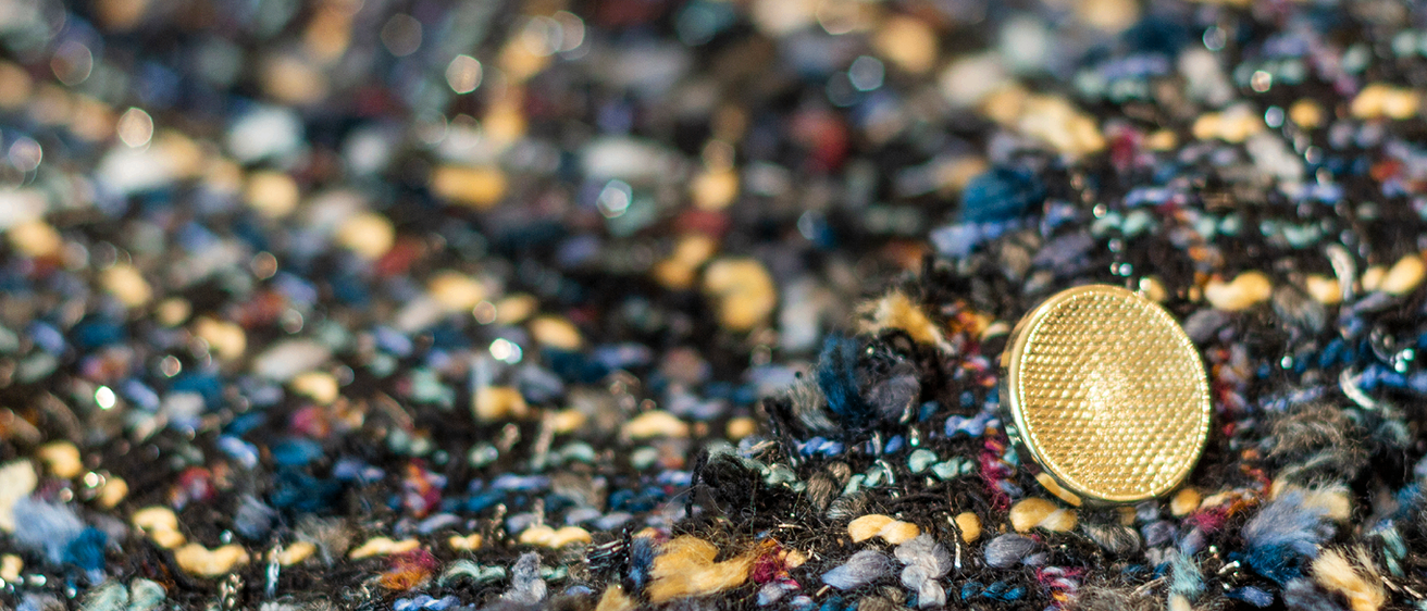 Eine Nahaufnahme eines strukturierten Stoffes, hauptsächlich in Blau und Schwarz, mit einer goldenen Knopf in der Vorderansicht. Der Stoff hat ein gewebtes Aussehen mit sichtbaren Fäden.