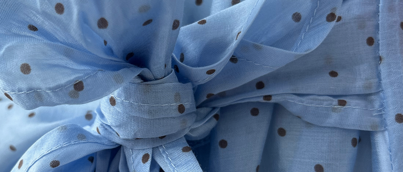 Ein Nahaufnahme eines blauen Stoffs mit braunen Punkten, der zu einem Bogen gebunden ist. Der Stoff ist glatt und glänzend und reflektiert Licht.