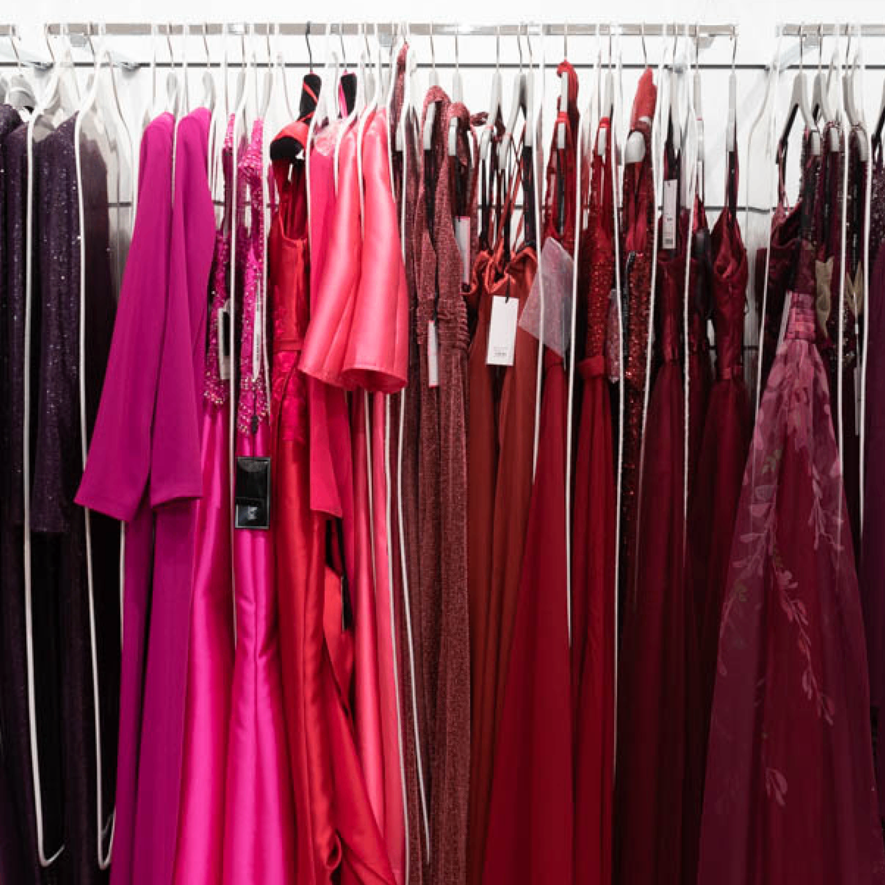Ein Kleiderständer mit Festkleidern in verschiedenen Farben wie pink, rot und braun hängt in einem Geschäft mit weißem Hintergrund.
