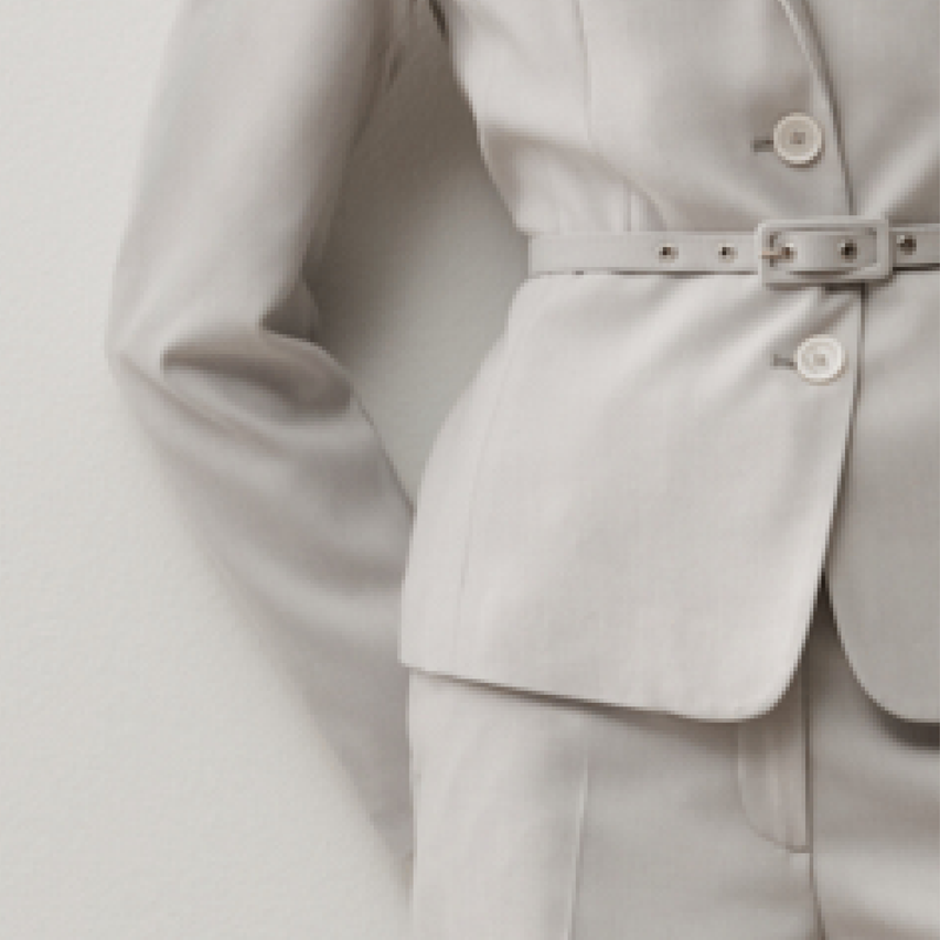 Eine Nahaufnahme eines hellen Anzugs mit Gürtel, weißen Knöpfen und einem Jackett mit langen Ärmeln.