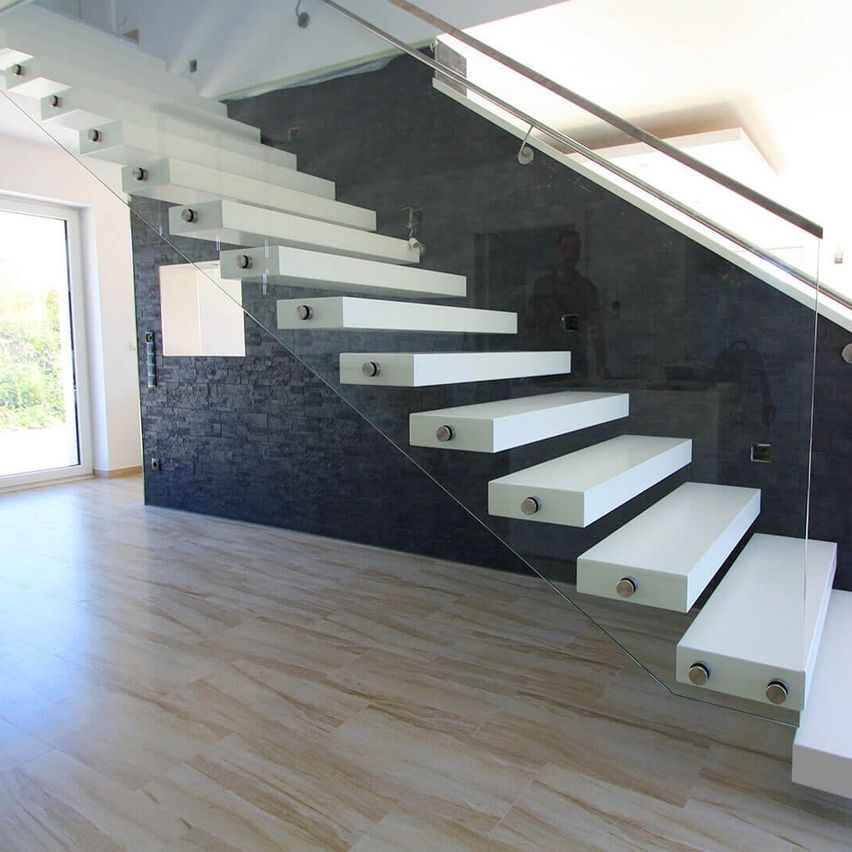 Eine moderne Glastreppe mit weißen Stufen und einer schwarzen Wand in einem leeren Raum mit Holzboden und Glastüren.