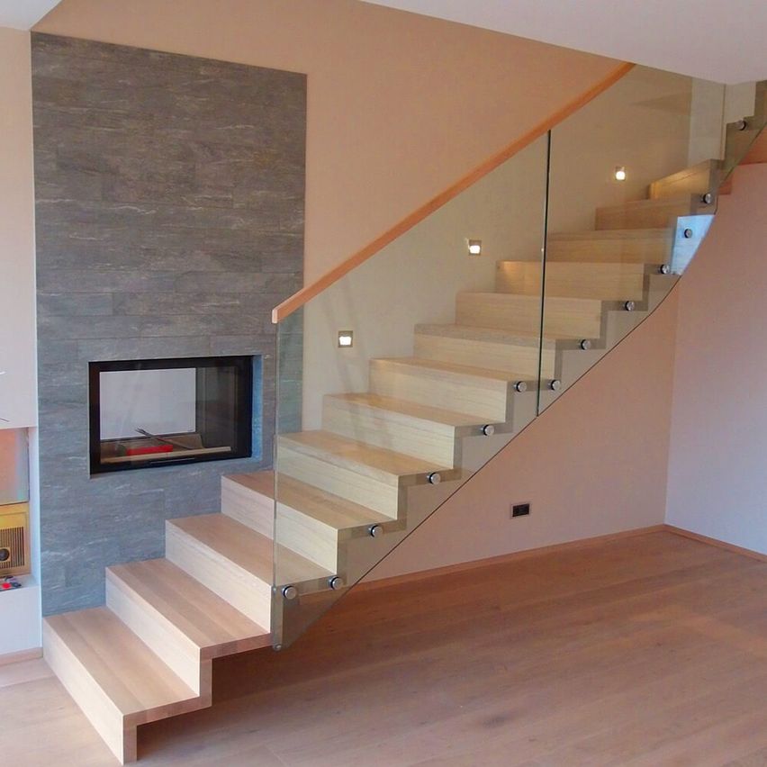 Moderne Treppe mit Glasgeländer und Holzstufen, neben einem Kamin mit Steinwand.