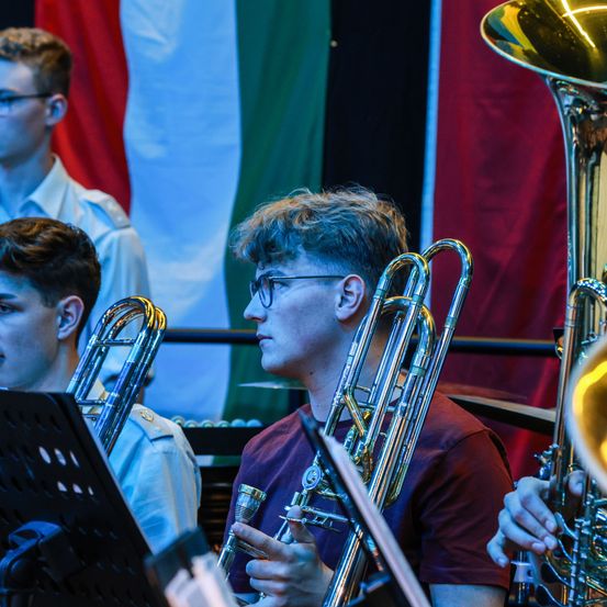 Ein Orchesterrehearsal mit mehreren Musikern. Im Hintergrund eine Flagge mit grün, weiß und roten Streifen.