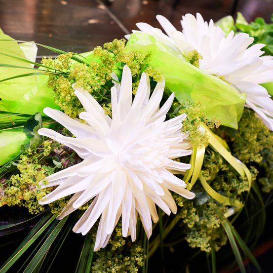 Eine Nahaufnahme von weißen künstlichen Blumen mit grünen Blättern und gelben Bändern. Die Blumen haben eine seidige Textur.