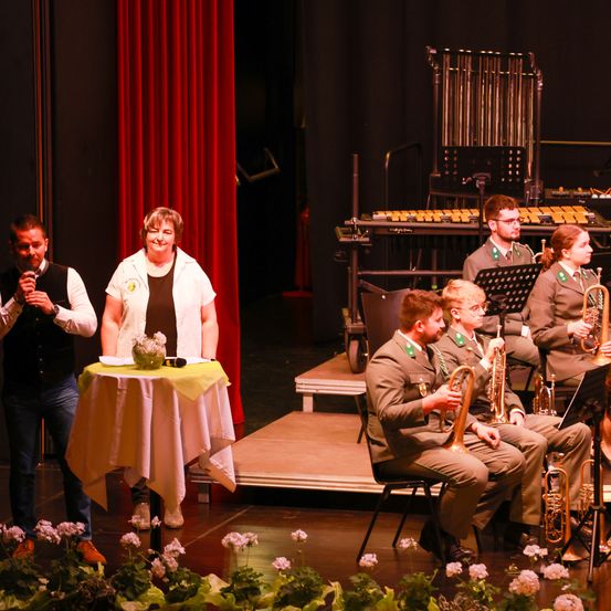 Eine Band spielt auf der Bühne vor einem roten Vorhang. Eine Frau hält ein Mikrofon und ein Mann spielt Trompete.