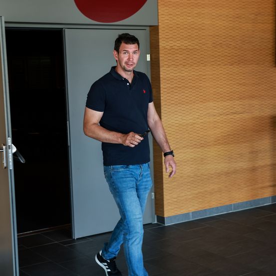Ein Mann in einem dunkelblauen Poloshirt und blauen Jeans geht durch eine offene Tür, möglicherweise um ein Gebäude zu betreten.