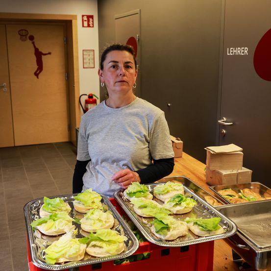Eine Frau steht hinter einem Tisch mit einem Tablett mit Sandwiches in einem Raum mit einem Basketballkorb an der Tür.