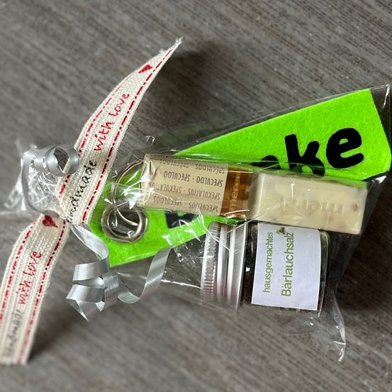 Ein Geschenkset mit Seife, Salz und Schlüsselanhänger, verpackt in Plastik mit einem Band, das mit Liebe geschrieben ist. Die Artikel haben Etiketten und ein grünes Schild, das Rauch sagt.