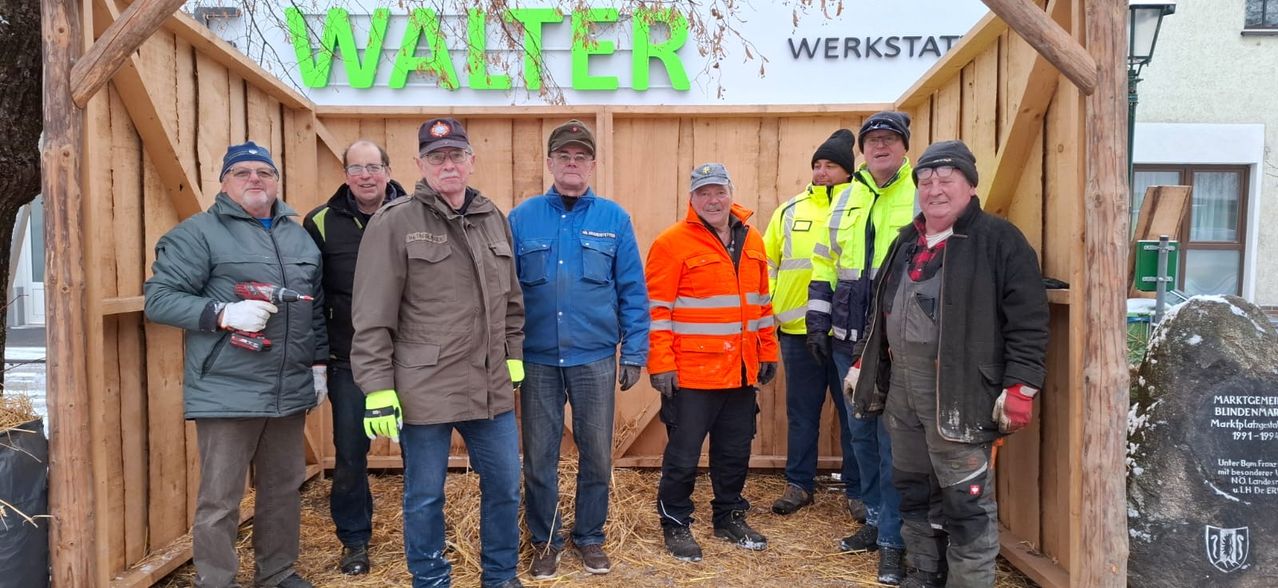 Eine Gruppe von Männern in Winterkleidung posiert für ein Foto vor einer Holzstruktur mit einem Schild, das 'Walter Werkstatt' liest.