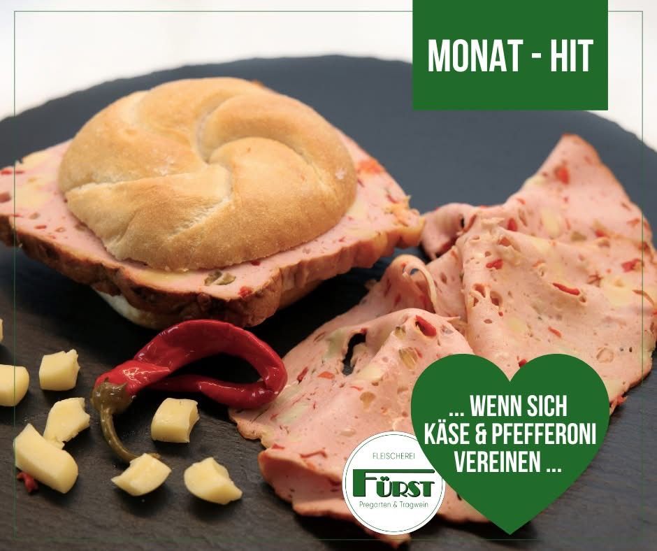 A sandwich with ham, cheese, and a red chili pepper is shown. The sandwich is on a black plate with a green heart-shaped background. The image is part of a promotional campaign.