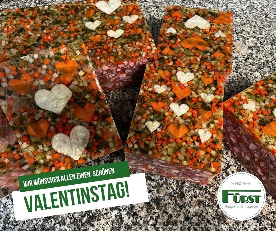A close-up of several slices of meat and vegetable jelly with heart shapes on a marble surface. A text reads 'Valentinstag!' on a green banner.