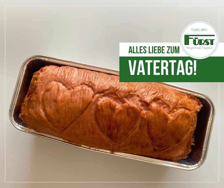 Ein Brotlaib mit goldbrauner Kruste in einer Metallpfanne auf weißem Hintergrund. Das Brot hat eine herzförmige Vertiefung auf der Oberseite. Ein grünes Banner sagt 'Alles Liebe zum Vatertag!', was 'Alles Liebe zum Vatertag!' bedeutet.