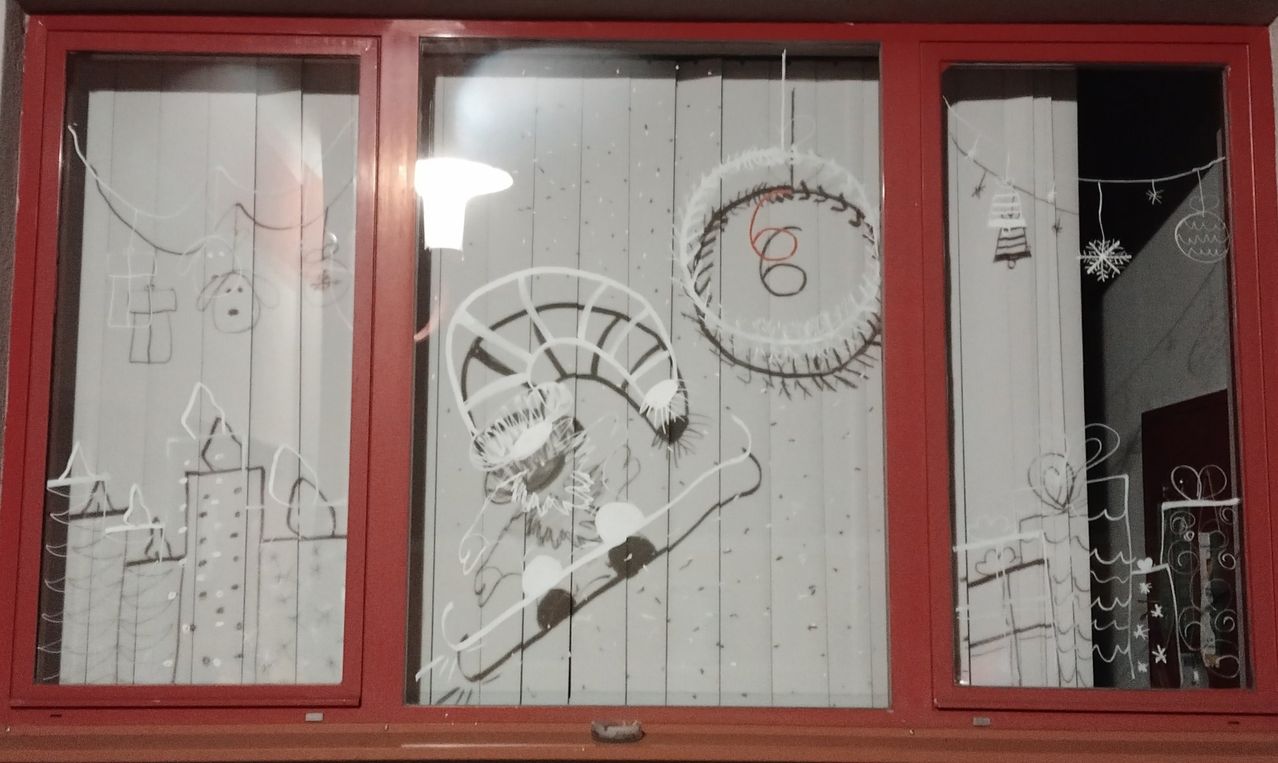 Ein roter Fensterrahmen zeigt eine Glasscheibe mit Graffiti, darunter ein Rad und die Zahl 6, sowie eine Blume und andere abstrakte Formen.