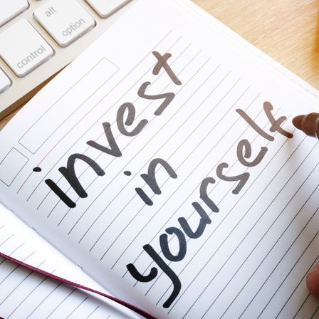 Ein offenes Notizbuch mit dem Wort Investiere in dich selbst darauf steht auf einem Schreibtisch mit einer Tastatur im Hintergrund.