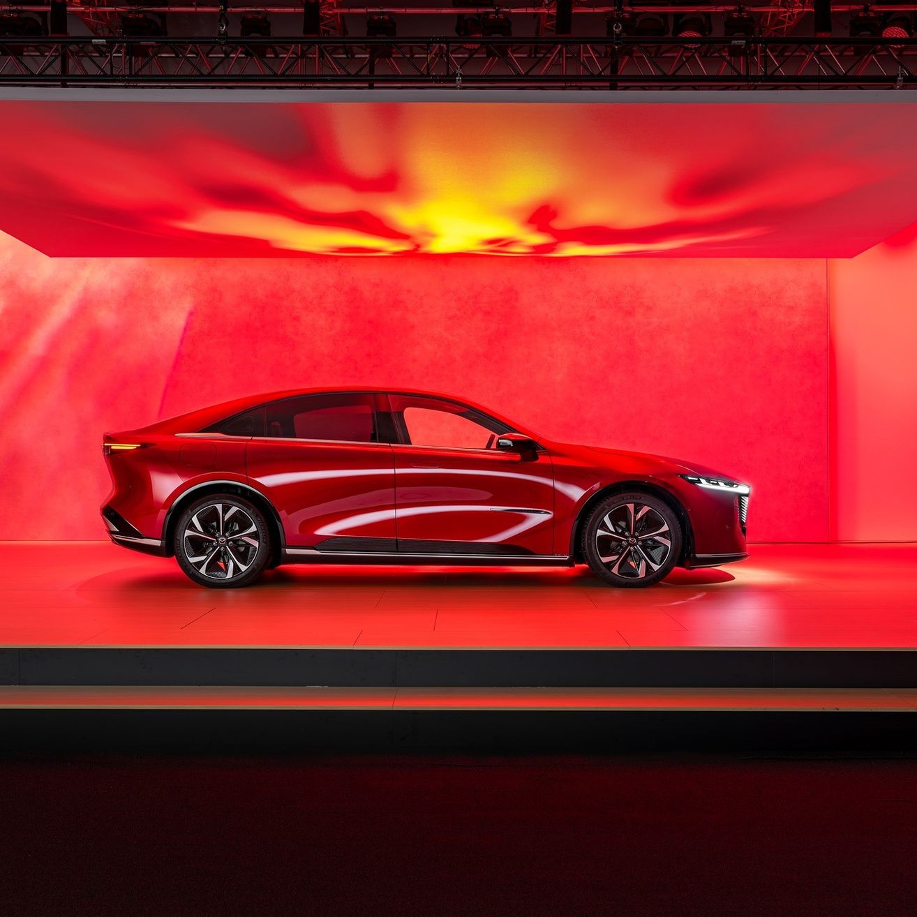 Ein rotes Auto wird in einem roten Raum mit gelber Beleuchtung darüber unter einem Scheinwerfer ausgestellt.