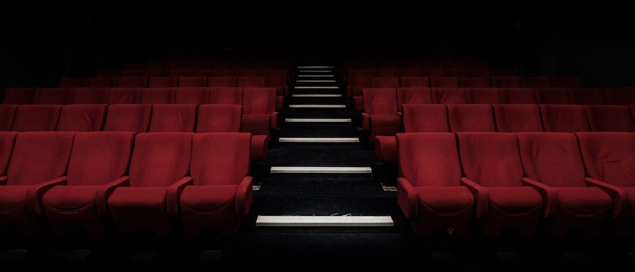 Ein leeres Kino mit roten Sitzen in Reihen und einer weißen Treppe, die nach vorne führt.