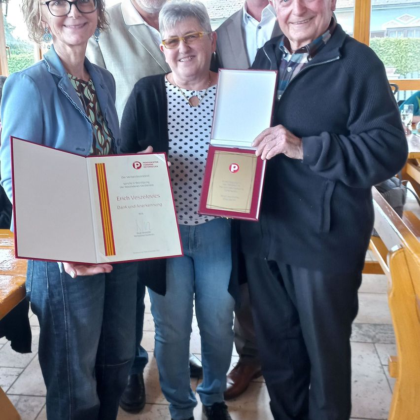 Vier Personen, zwei Frauen und zwei Männer, halten Zertifikate. Sie lächeln und stehen zusammen in einem Raum.