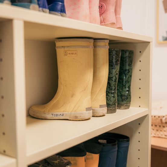 Ein weißer Regalboden hält eine Reihe von Stiefeln, darunter ein gelber, der mit Tobias beschriftet ist, und andere farbige Stiefel.