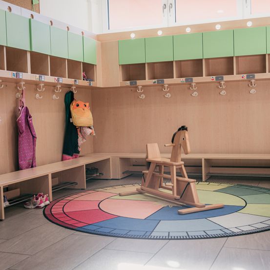 Ein Kinderzimmer mit Spinden und einem Teppich mit einem Holzpferd, mit bunten Fächern und Bänken an der Wand.