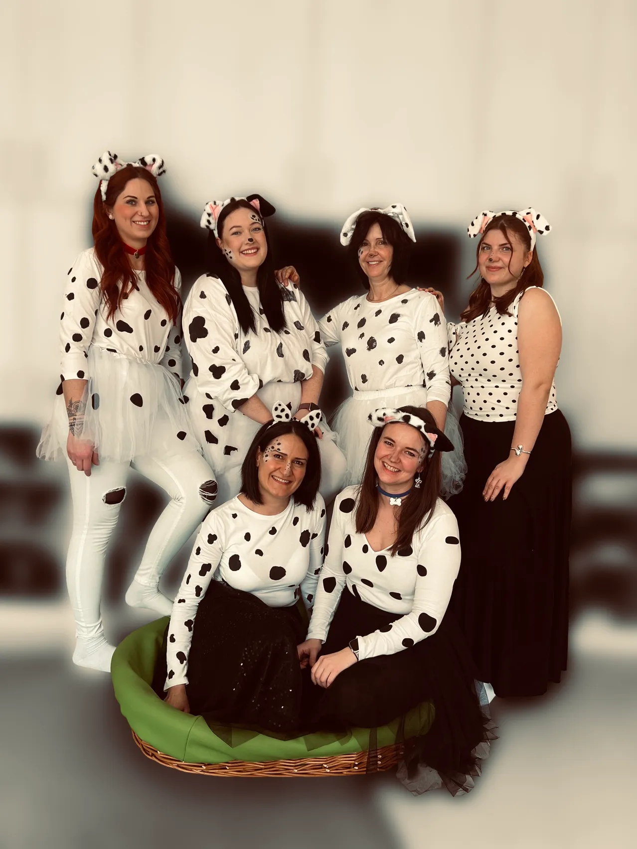 Eine Gruppe erwachsener Frauen in Dalmatiner-Kostümen, eine sitzt in einem grünen Korb, lächelt und posiert für ein Foto.