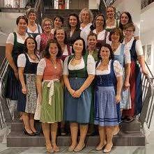 Eine Gruppe von Frauen in traditioneller bayerischer Kleidung, einschließlich Dirndln, posiert für ein Foto auf einer Treppe.