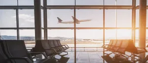 Ein leerer Flughafenterminal mit Glaswänden, die ein Flugzeug im Hintergrund beim Start zeigen.