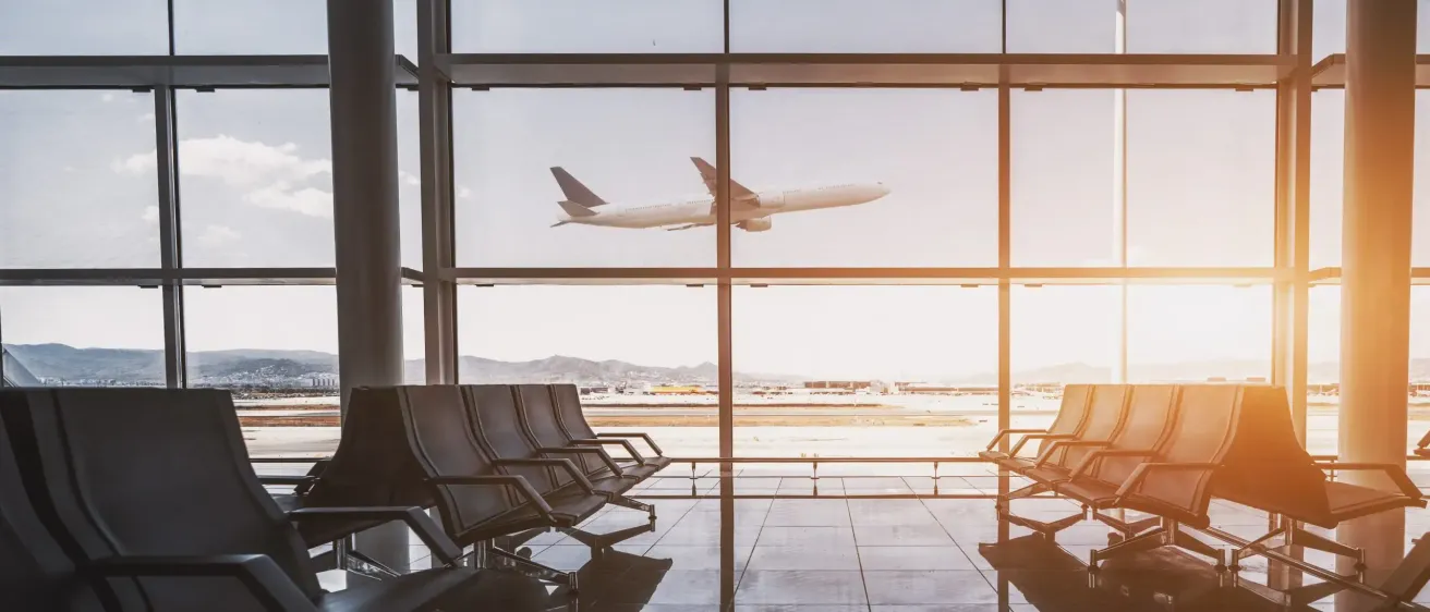 Ein leerer Flughafenterminal mit Glaswänden, die ein Flugzeug im Hintergrund beim Start zeigen.