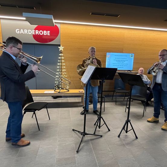 Vier Musiker treten in einem Raum auf. Drei stehen vor Musikständern, einer steht links. Dahinter befindet sich ein Weihnachtsbaum mit einem Stern oben.