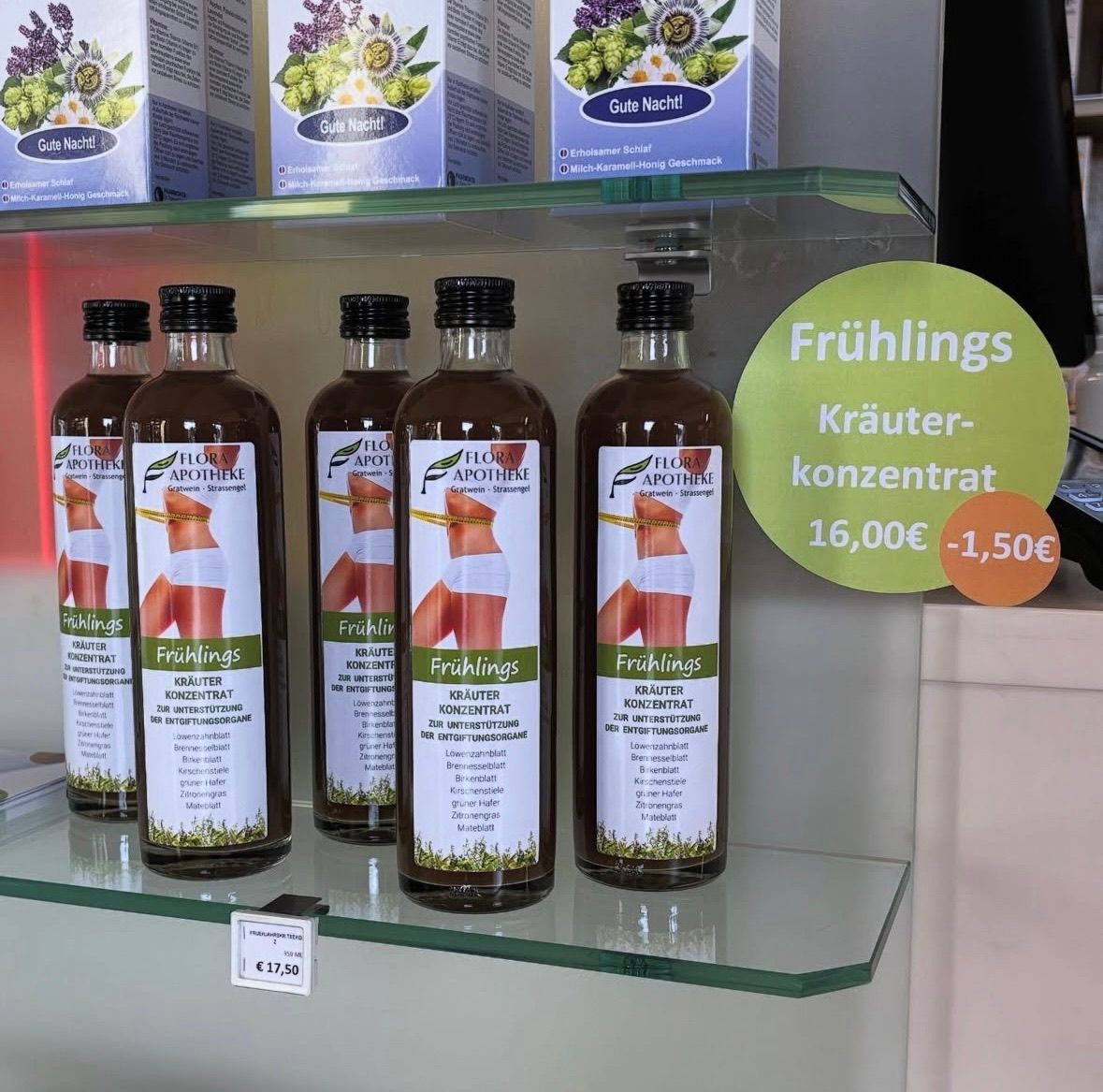 Fünf Glasflaschen mit Fruhlings-Kräuterkonzentrat, gekennzeichnet und mit Preisschildern, darüber ein Schild mit der Aufschrift Fruhlings Kräuter-Konzentrat 16,00 Euro - 1,50 Euro