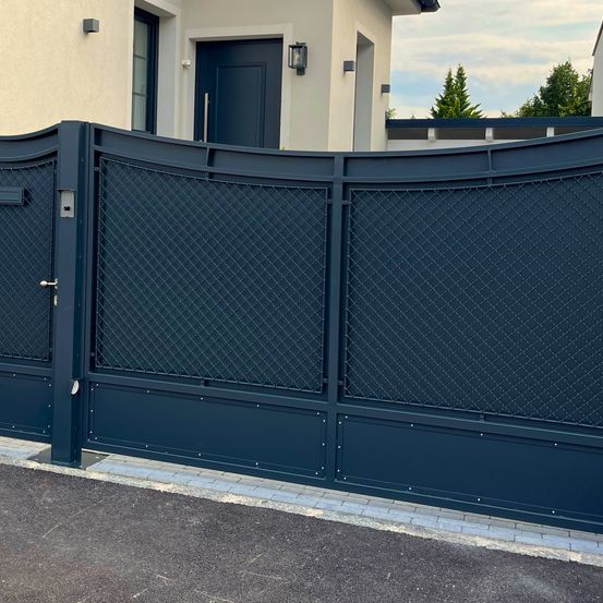 Ein navyblaues Metalltor mit Gitterdesign vor einem Haus. Das Tor ist mit einem Schloss verschlossen.