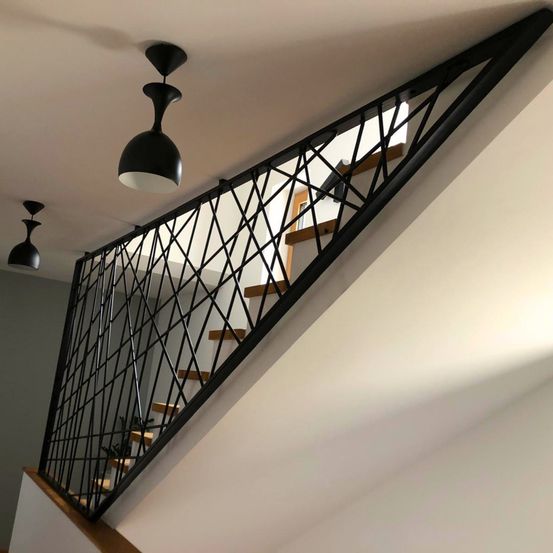 Eine moderne Treppe mit schwarzem Metallgeländer, mit geometrischem Design und zwei schwarzen Pendelleuchten an der Decke.