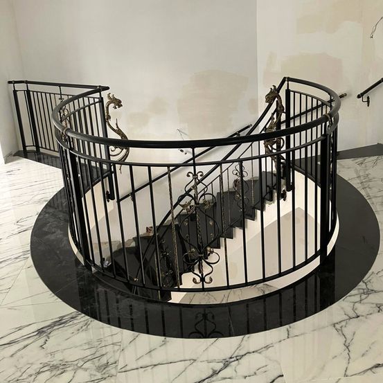 Eine schwarze Wendeltreppe mit Marmorboden und weißer Wand. Die Geländer haben goldene Drachendesigns.