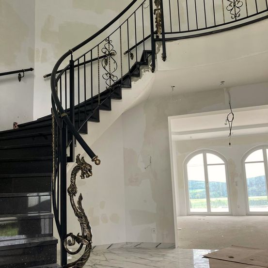 Ein Haus mit einer Wendeltreppe und weißen Wänden. Die Treppe hat ein Drachendesign an ihrem Geländer. Das Haus hat einen Blick nach draußen durch die Fenster.