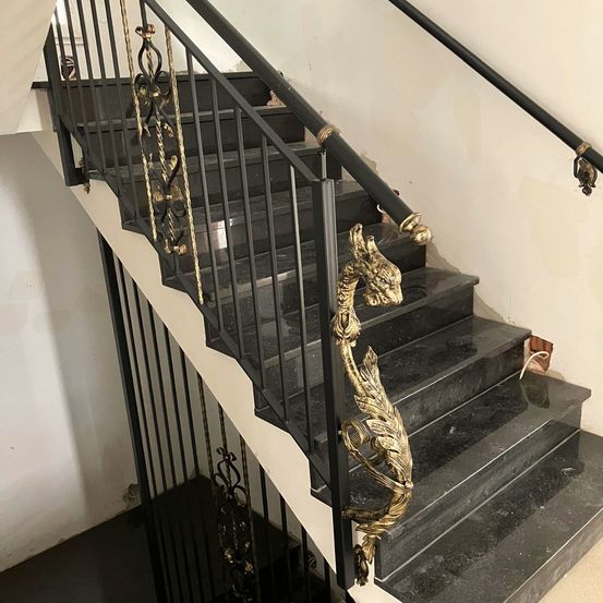 Eine schwarze Marmortreppe mit kunstvollen goldenen Geländern. Die Stufen haben einen glatten, glänzenden Abschluss.