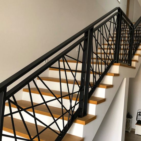 Eine moderne Treppe mit schwarzen Metallgeländern und Holzstufen. Das Design ist schlank mit geometrischen Mustern. Der Raum ist gut beleuchtet und hat weiße Wände.