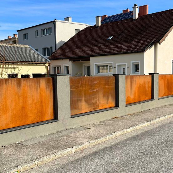 Ein Haus mit einem braunen Dach und Solarpanelen darauf. Es hat eine braune Einfriedung vorn.