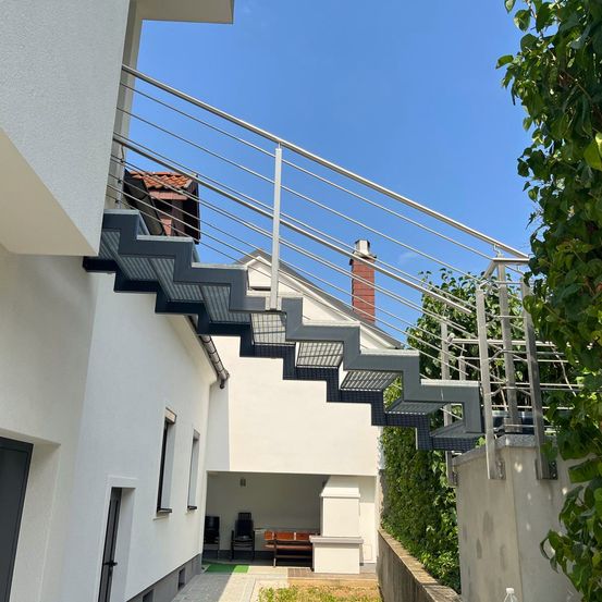 Ein modernes Haus mit einer Metalltreppe und Geländer, mit Blick auf einen Hinterhof mit einer Holzbank und einem Schornstein.