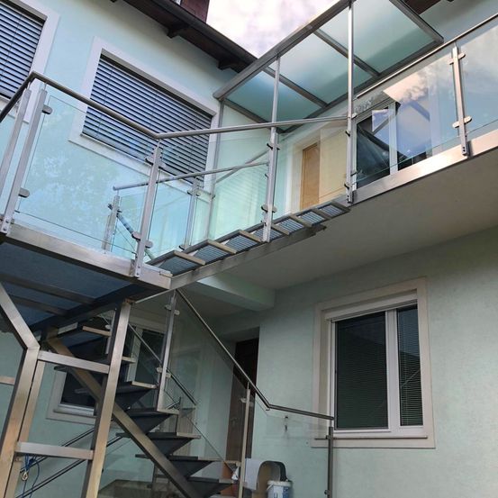 Ein Gebäude mit Glasgeländer, Treppe und Glasfenstern. Das Haus hat Metallgeländer und eine Glasüberdachung. Die Treppe ist aus Metall und Glas.