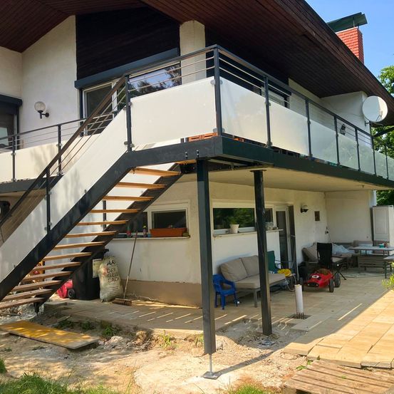Ein Haus mit einem Balkon im Obergeschoss, eine Treppe, die hinauf führt, und ein Terrassenbereich mit Möbeln.