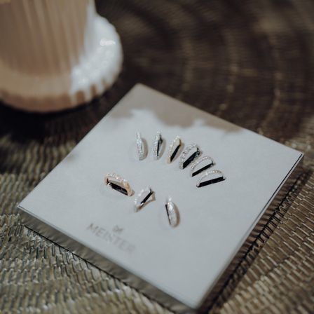 Eine weiße Präsentationsbox mit mehreren Silberringen und Ohrringen von Menster liegt auf einer gewebten Oberfläche.