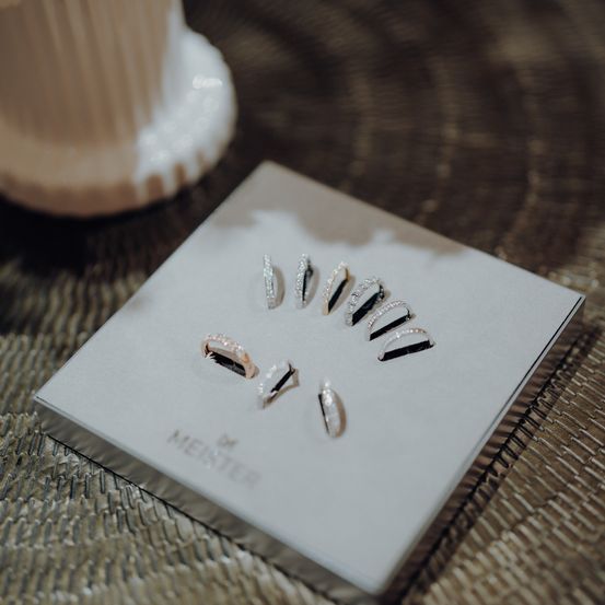Eine weiße Präsentationsbox mit mehreren Silberringen und Ohrringen von Menster liegt auf einer gewebten Oberfläche.
