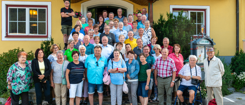 Eine große Gruppe von Menschen posiert für ein Foto vor einem gelben Gebäude, das mit Restaurant beschriftet ist.