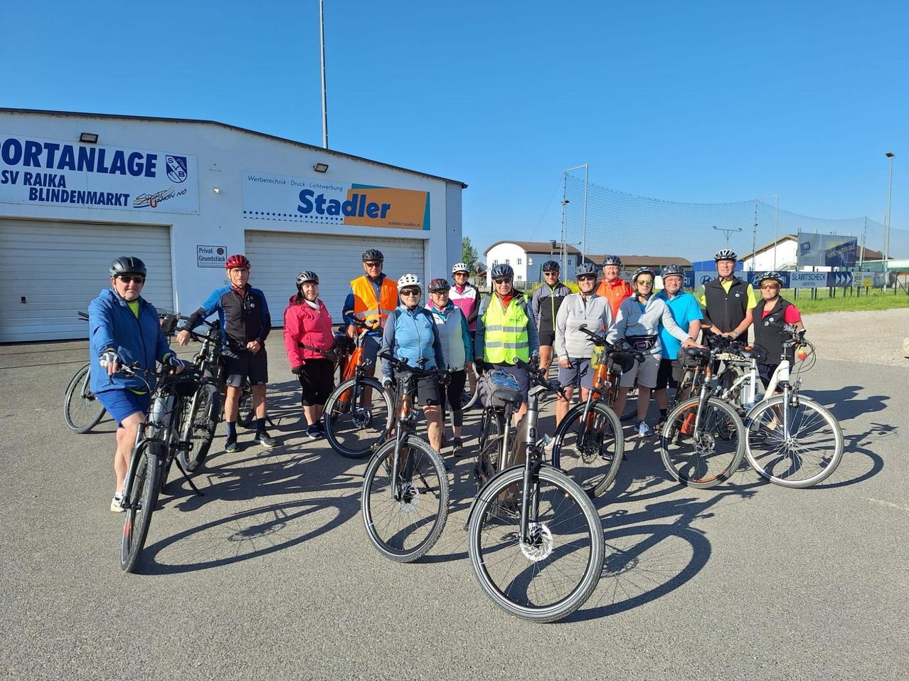 Eine Gruppe von Radfahrern, alle mit Helmen, posiert für ein Foto vor einem Gebäude mit dem Namen Stadler.