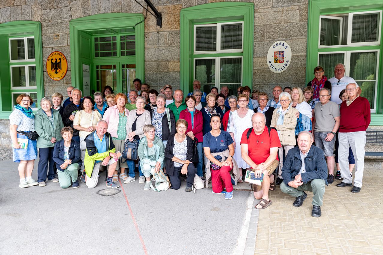 Eine Gruppe älterer Menschen posiert für ein Foto vor einem Gebäude mit grünen Fenstern und einem Schild, das Ceska Republika steht.